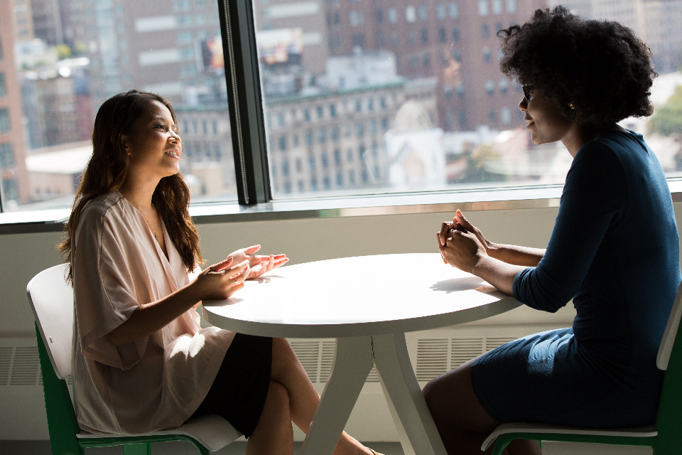 Two people in conversation across a table by an office window